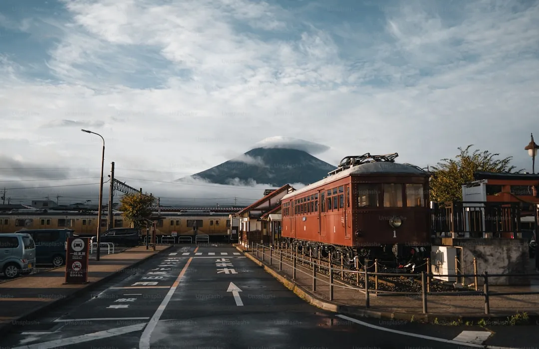 曇り空の下、山を背に停まる赤い車両の列車